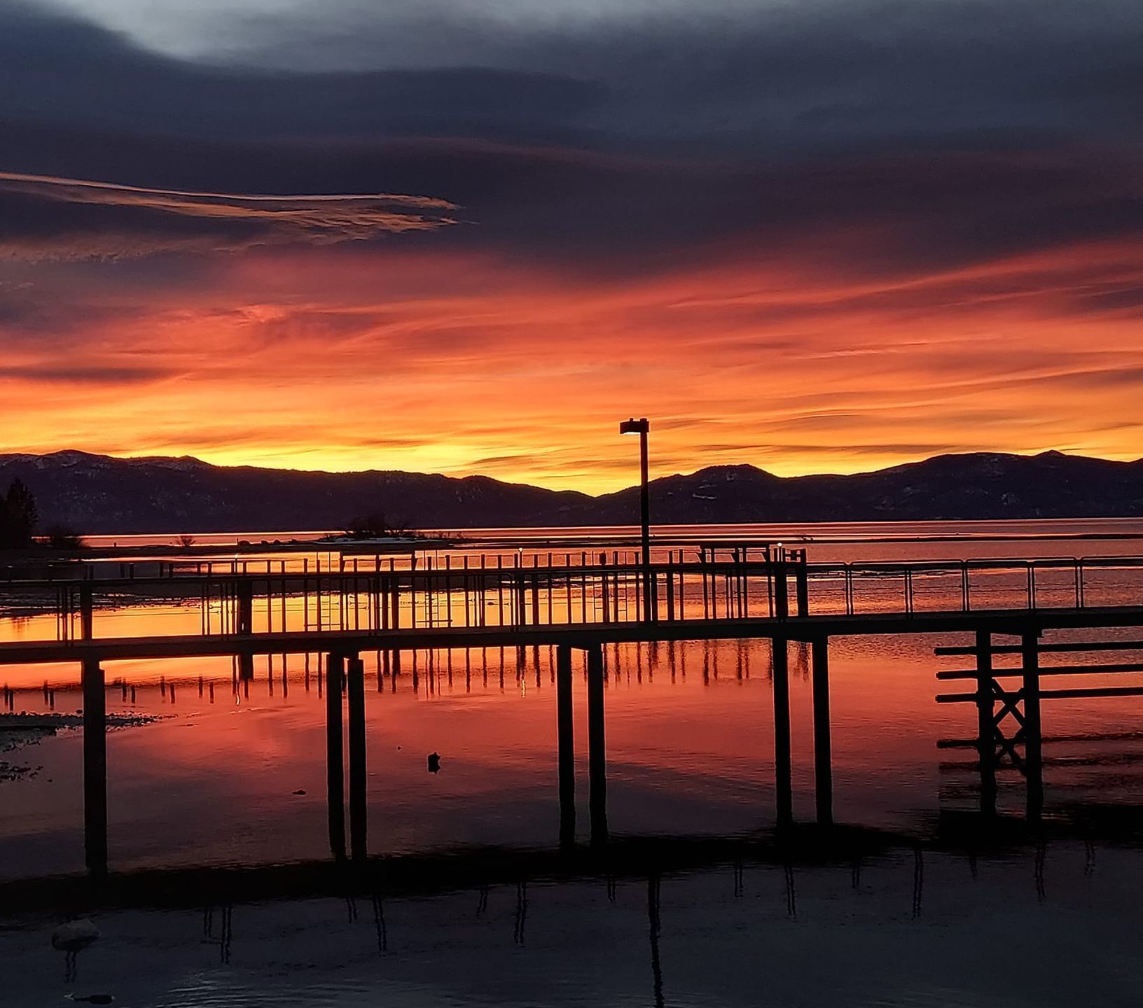 Sunset over water with pier silhouetted against vibrant orange and red sky.