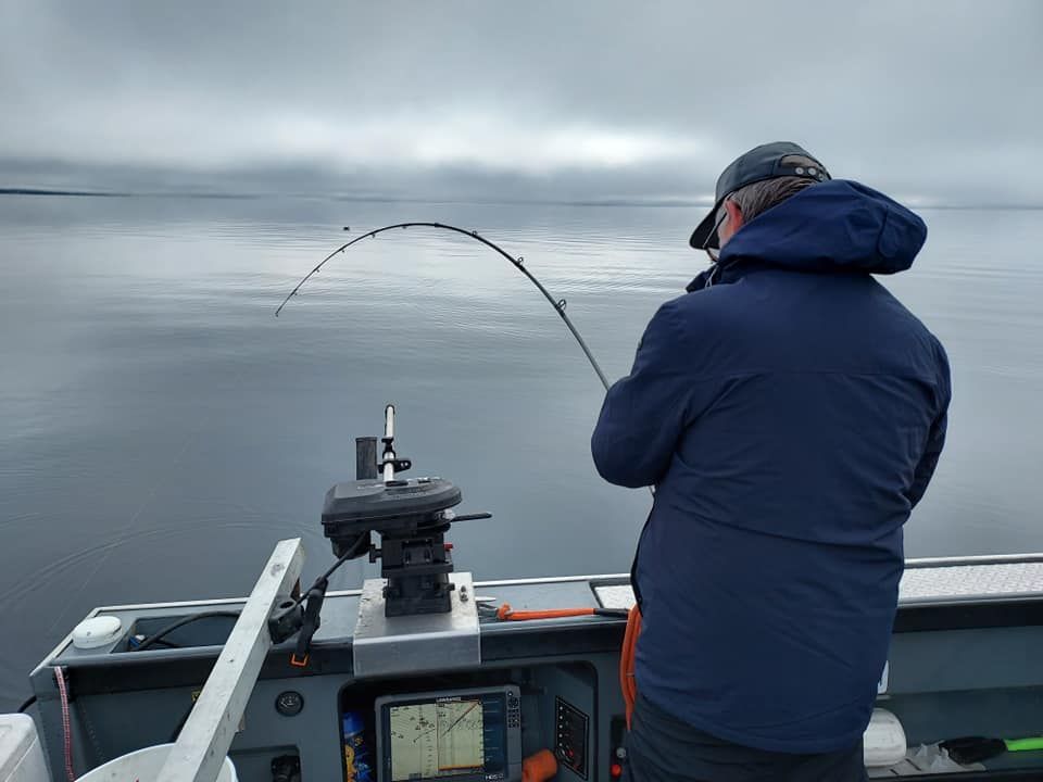 Person fishing from a boat, holding a bent fishing rod, cloudy water in the background.