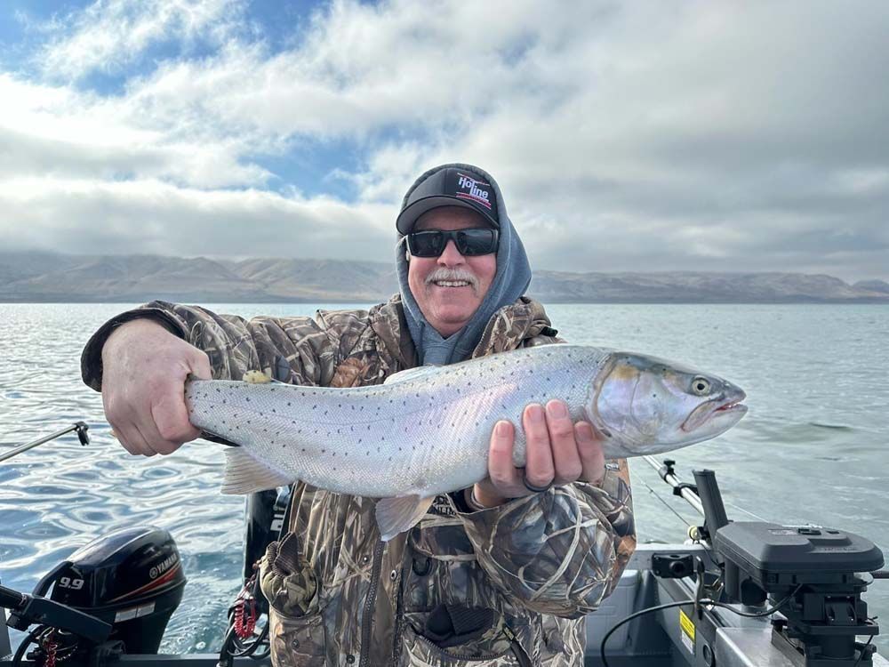 Man on a boat holding a large, speckled fish.