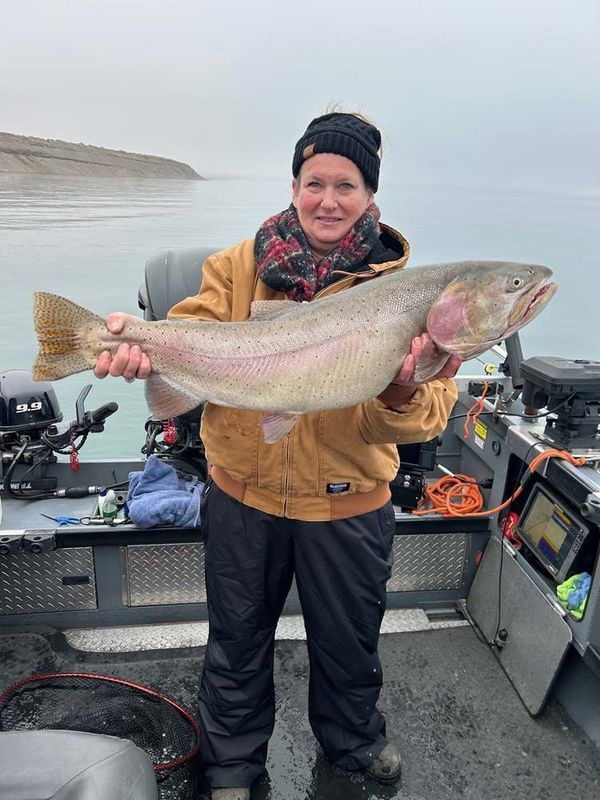 Woman on boat holds large rainbow trout.