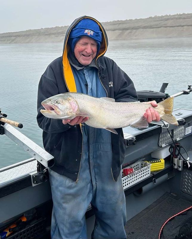 Man in blue and black fishing gear holds a large, silver fish on a boat.