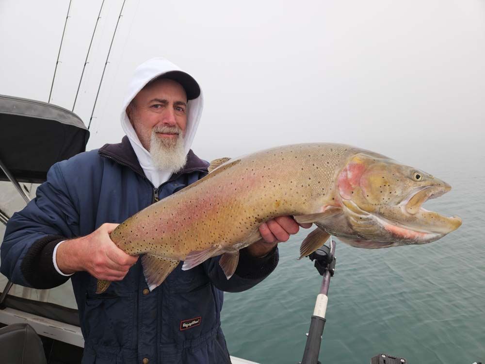 Man holding large trout on a boat in a foggy setting. 