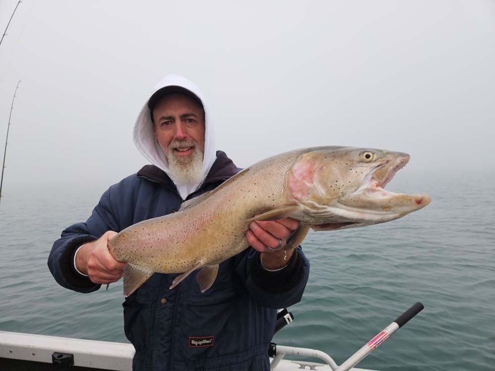 Man holding large fish, open mouth, on boat, foggy water.