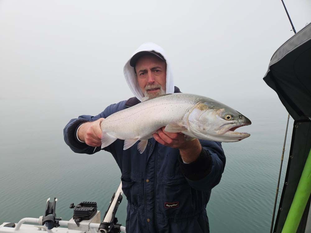 Man holding a silver fish on a boat in foggy water.