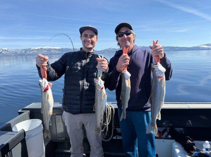 Two men on a boat, holding up caught fish. 