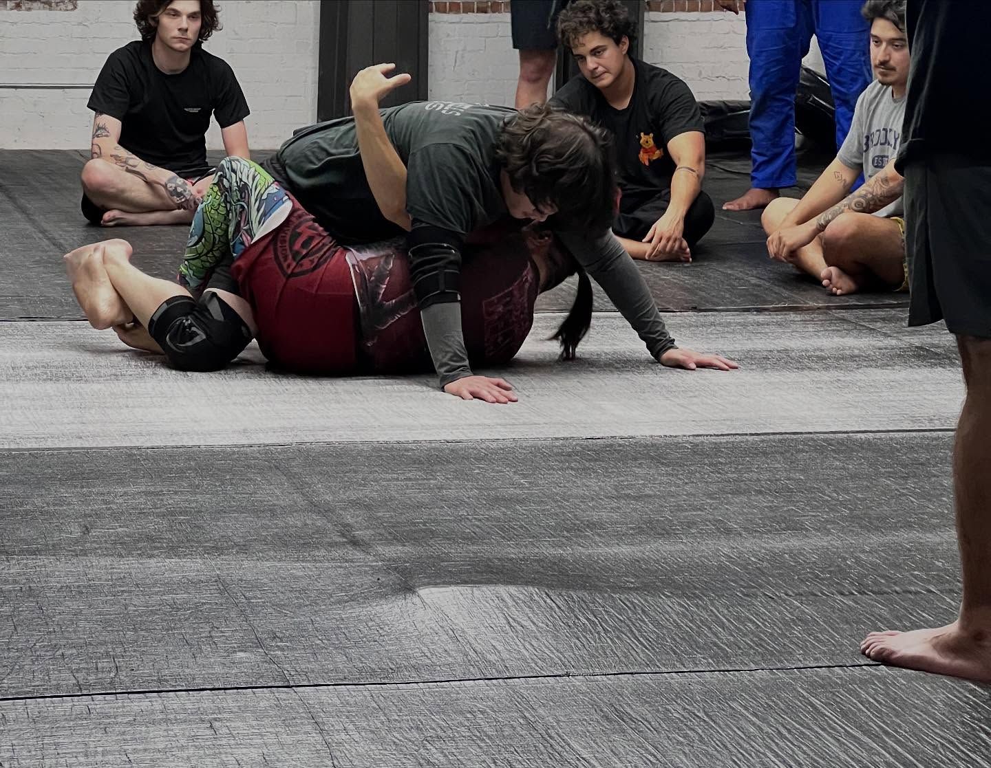 People practicing a wrestling move on a street while others watch nearby