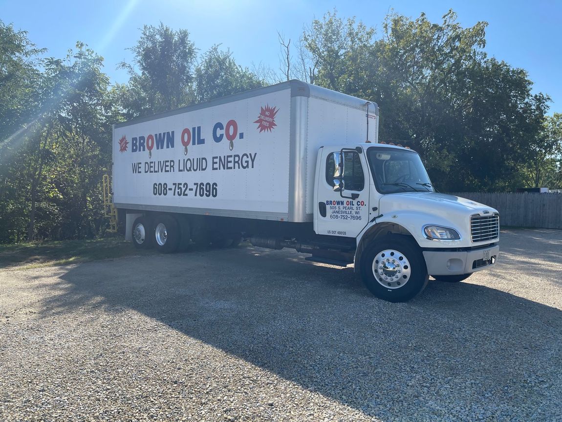 A brown oil co. truck is parked in a gravel lot