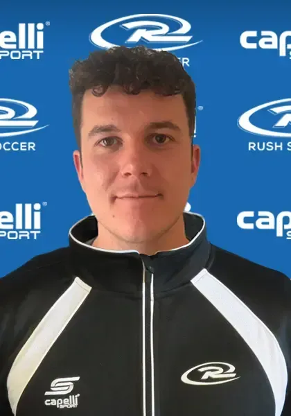 Man wearing a black and white track jacket, smiling at the camera, with a blue background and sports logos.