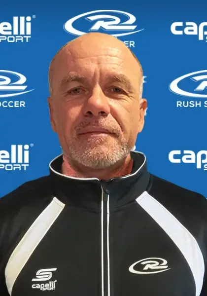 Bald man in a black and white track jacket, posing in front of a blue background with logos.