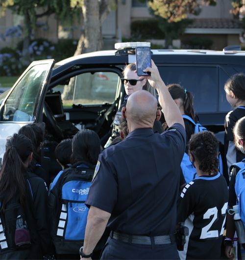 Police officer taking a photo of a group of students in front of a police vehicle.