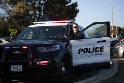 Police officer standing next to a patrol car with open door. 