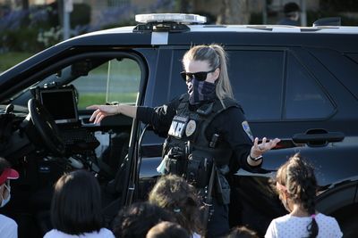 Police officer in uniform talking to a group of children near a patrol car.