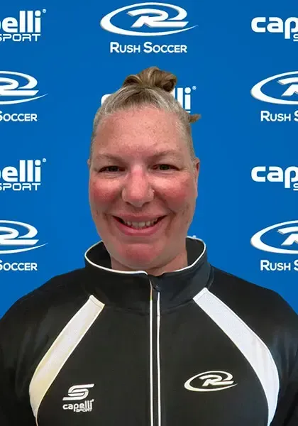 Woman in a black and white athletic jacket smiles, standing in front of a blue background with soccer team logos.
