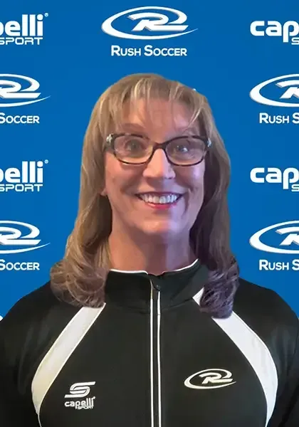 Woman wearing glasses, a black and white jacket, smiling in front of a blue background with soccer logos.