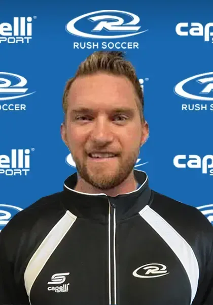 Man with short, light brown hair and a beard, smiling in front of a blue backdrop with 