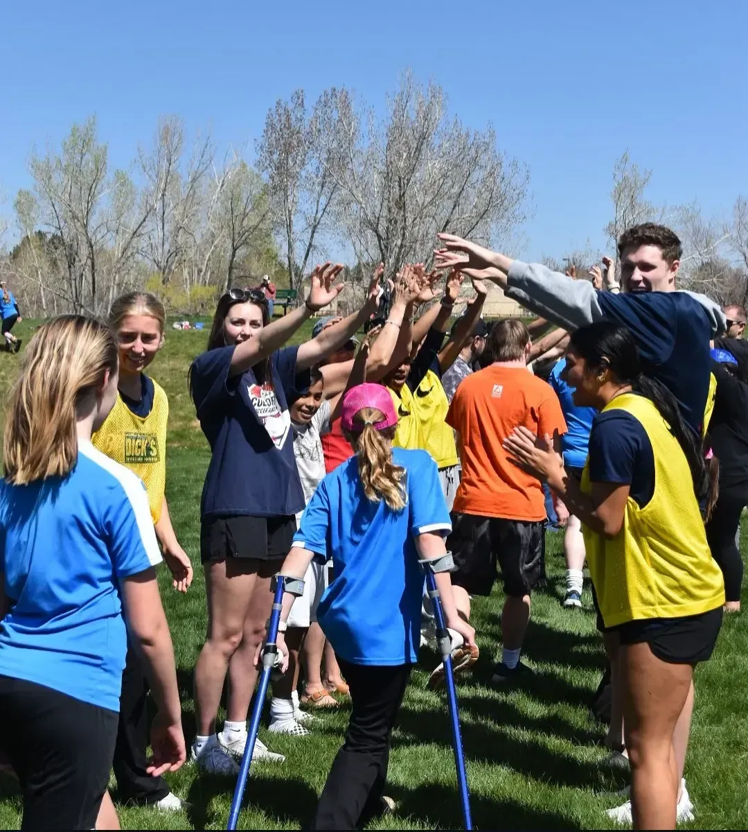People high-fiving in a park. A person with crutches walks toward the group.