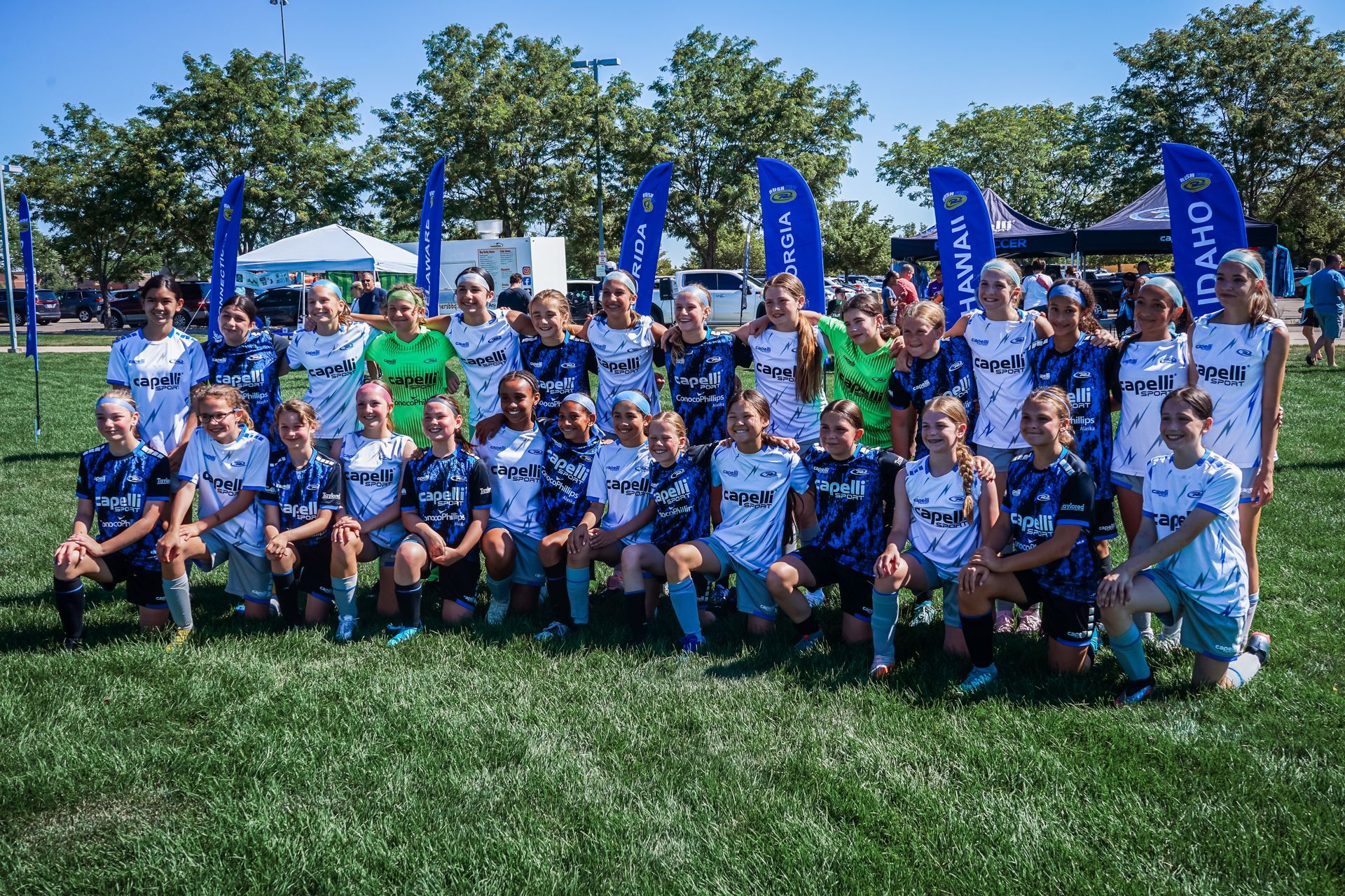 Youth soccer team posing on a grass field, wearing blue and white uniforms.