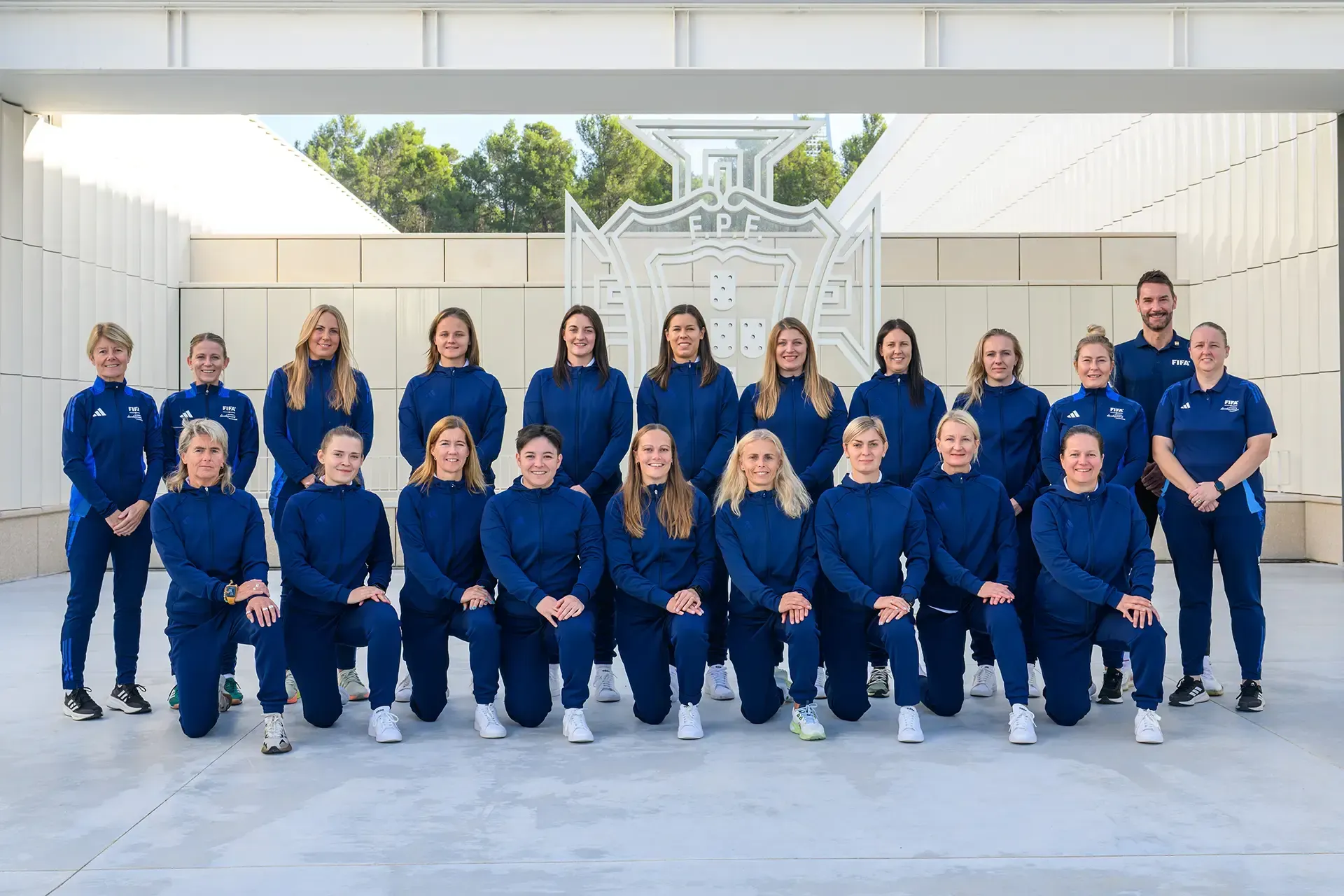 Group of people in matching blue tracksuits posing outdoors in front of a modern building.