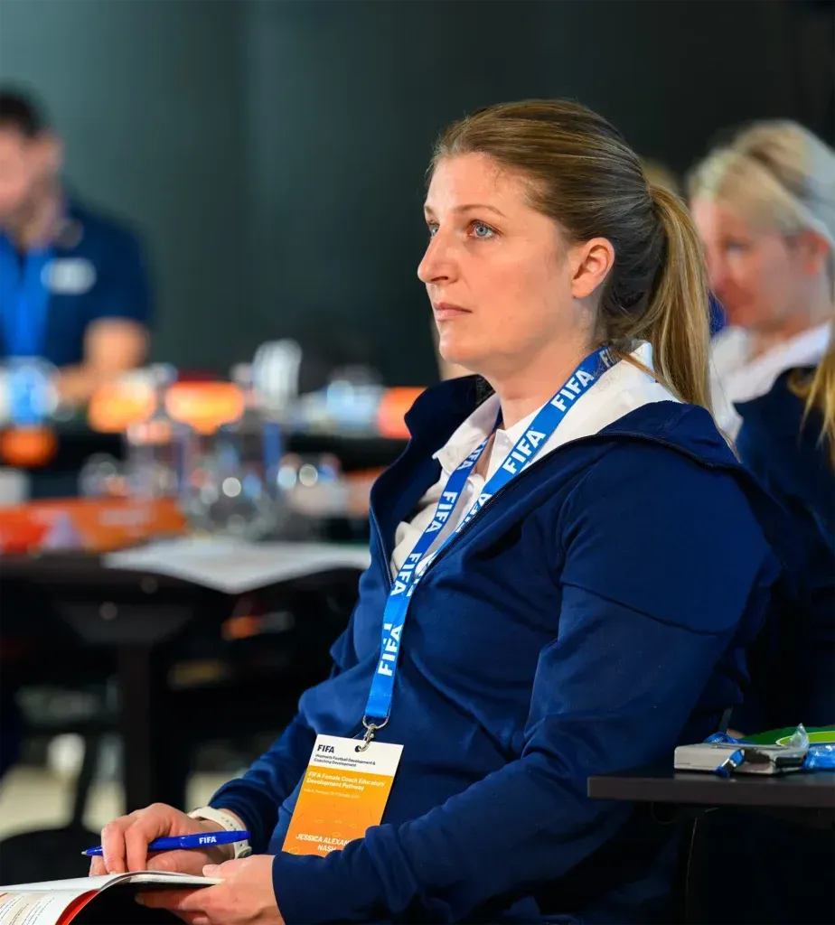 Woman in blue jacket, attending a conference, looking intently.