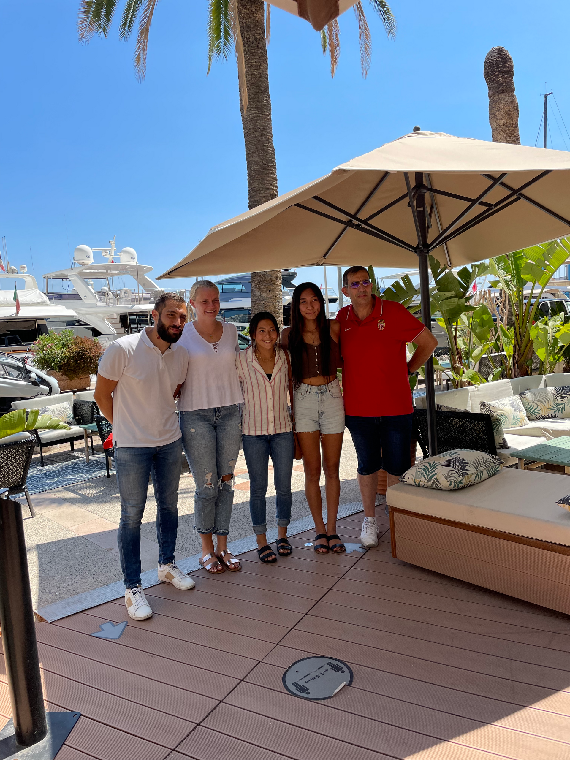 Five people stand posing outdoors near a waterfront.