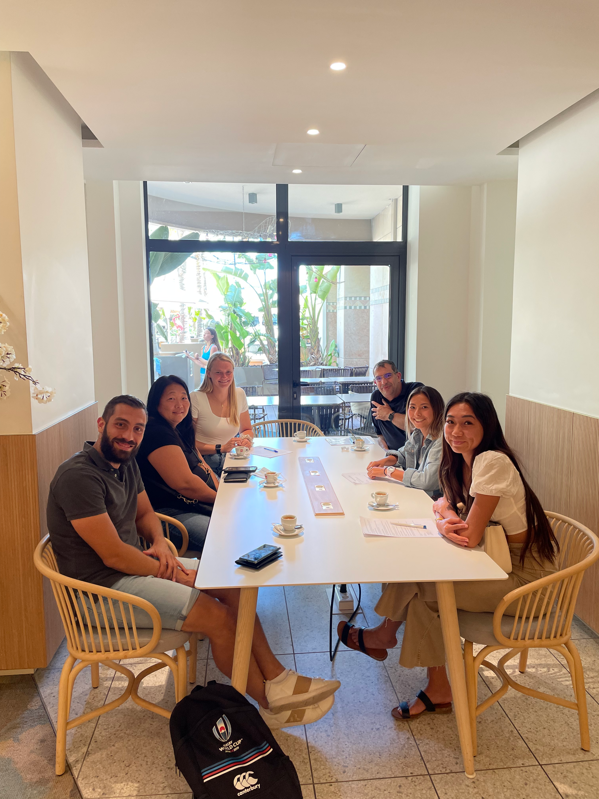 Group of people seated at a white table in a cafe, looking at the camera.