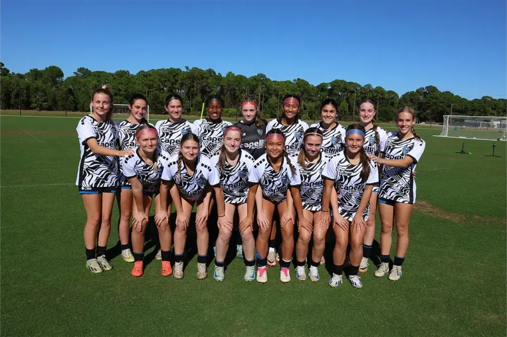 Soccer team posing on a green field wearing matching jerseys in front of trees under a clear sky.