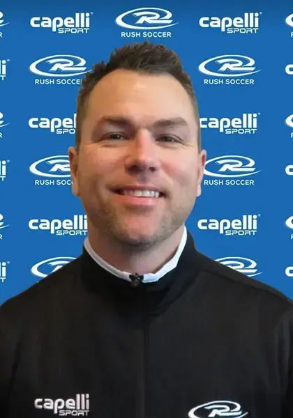 Man smiling, wearing a black shirt, in front of a blue backdrop with sports-related logos.