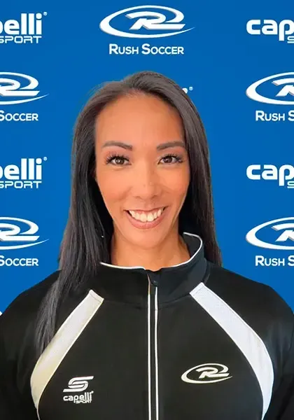 Woman with dark hair smiling, wearing a black athletic jacket with white accents. Background features sports logos.