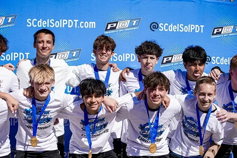 A team of young men in white shirts with medals posing together, smiling in front of a blue backdrop.