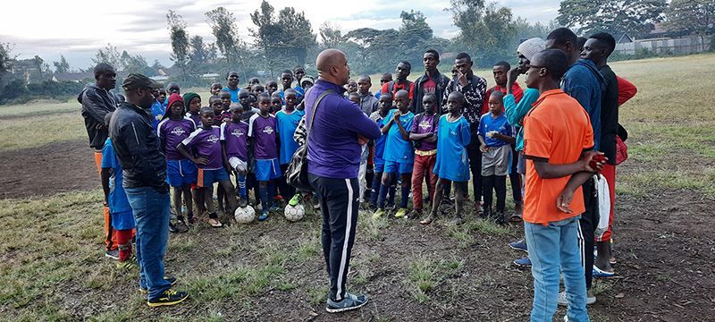 A group of children in sports attire listen to a coach on a field.