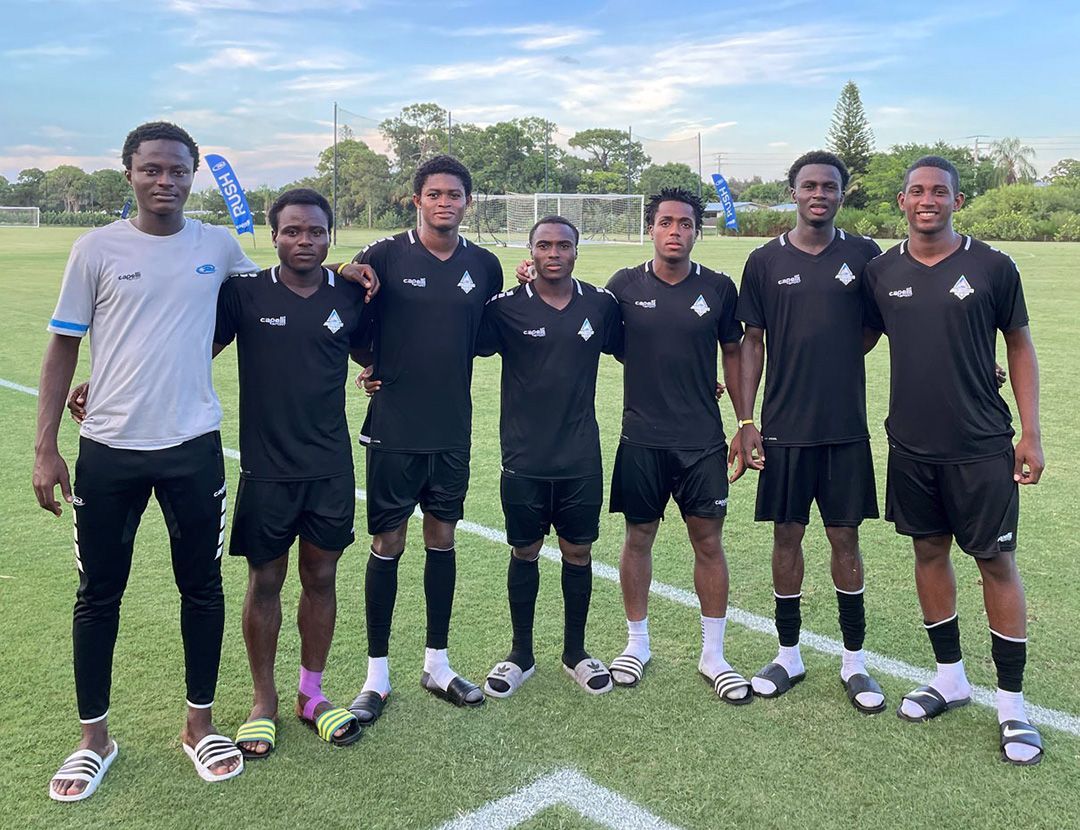 Seven soccer players in black uniforms standing on a green field.