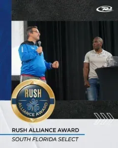 Man in blue speaks at podium, other man beside him. Award banner reads 
