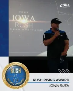 Man in black cap and blue shirt speaks at podium with 