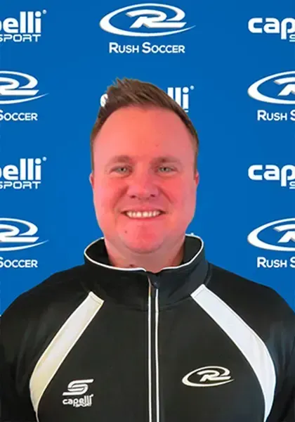 Man smiling, wearing a black and white track jacket, in front of a blue background with soccer logos.
