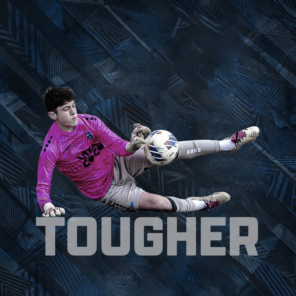 A goalkeeper in a pink jersey dives horizontally to save a soccer ball against a dark, patterned background.