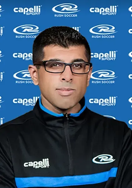 Man wearing glasses and athletic jacket against a Rush Soccer backdrop.