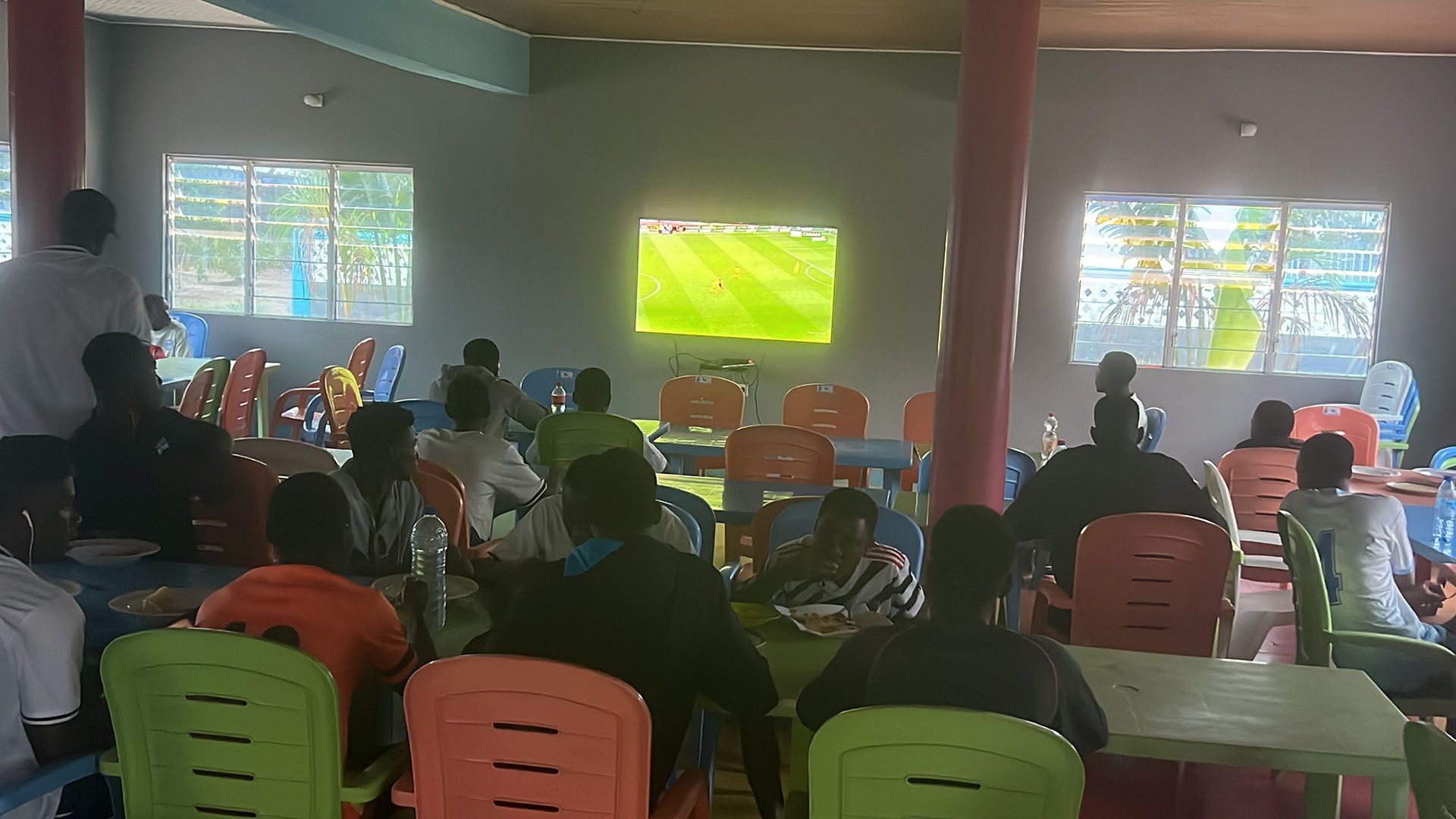 People watching a soccer match on a TV in a dining area with tables and chairs.
