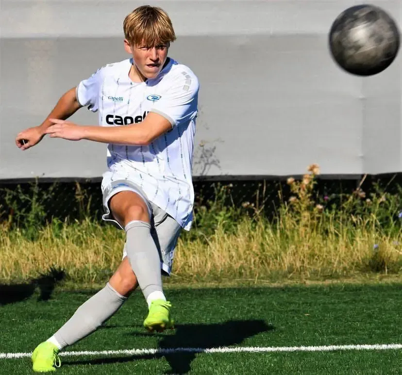 Soccer player in white uniform kicking ball on green field.