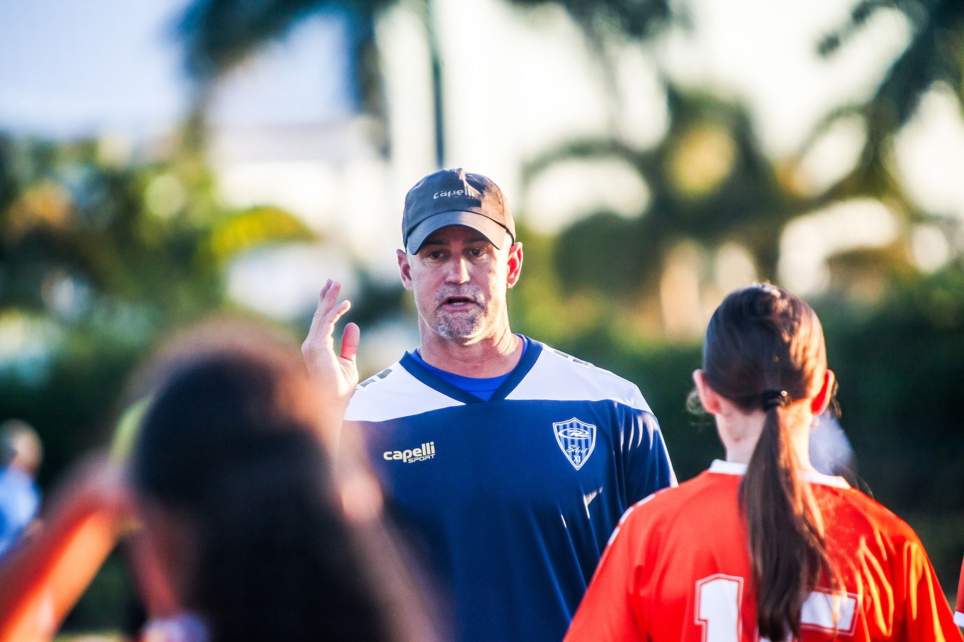 A coach talks to a team of young players on the bench during a soccer game. They're wearing green and black uniforms.