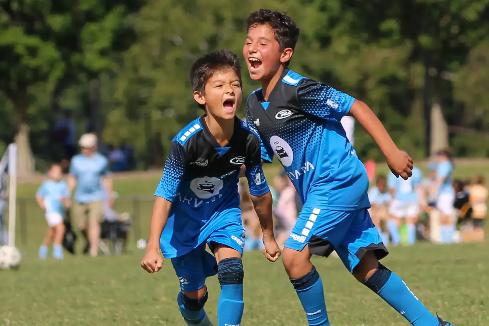 Two boys in blue soccer uniforms celebrate on a field, cheering with excitement.