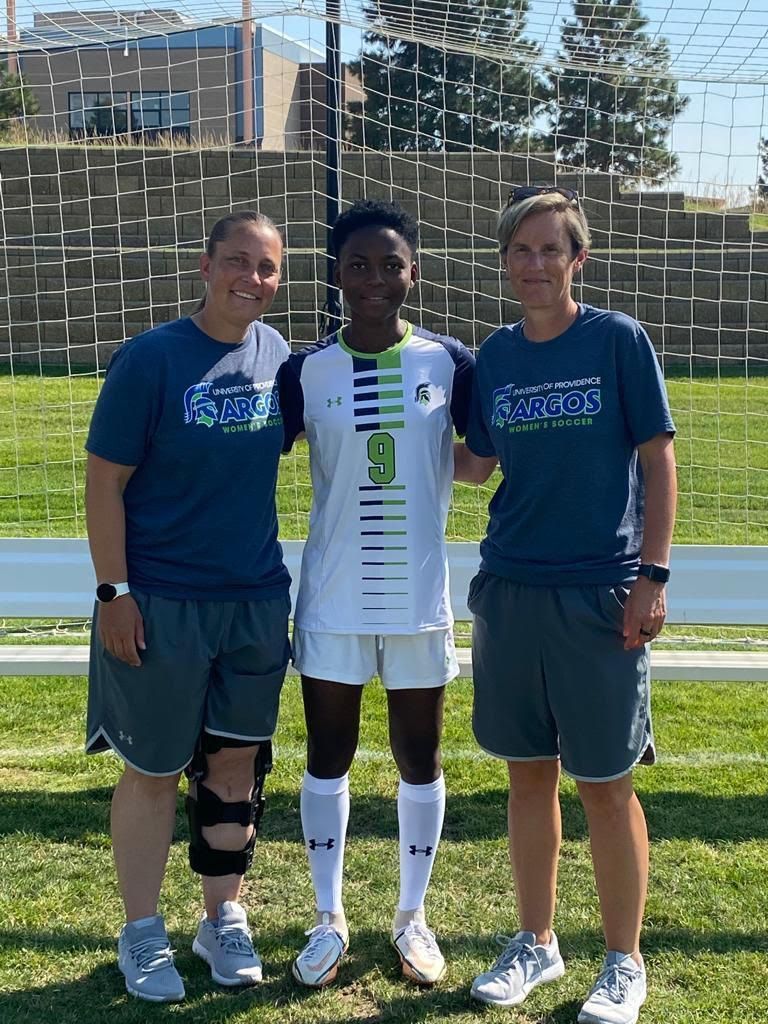 Soccer player with coaches, standing on field. Player in white jersey, coaches in blue shirts.