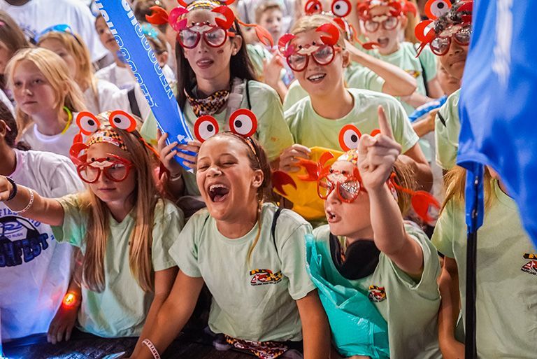 Group of people wearing crab-shaped glasses, cheering, with light green shirts.