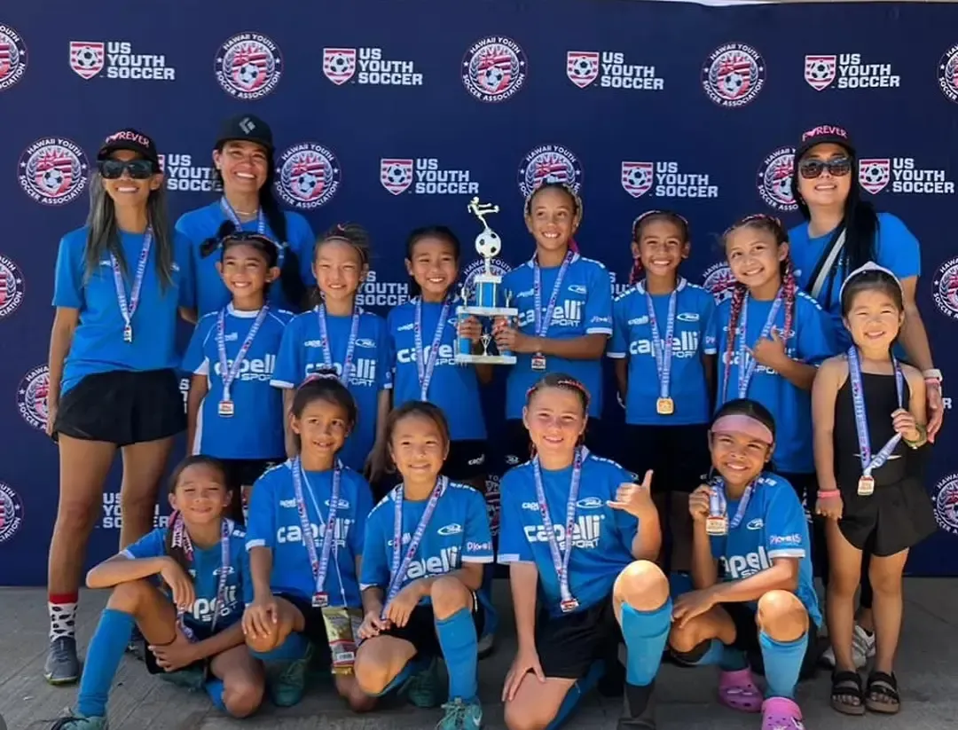 Youth soccer team in blue uniforms holding a trophy, posing for photo.