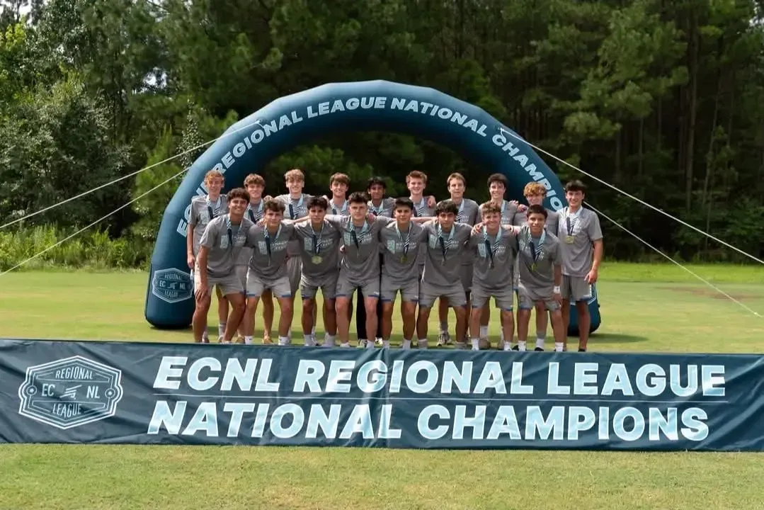 Soccer team posing with medals and banner, celebrating ECNL Regional League National Champions.