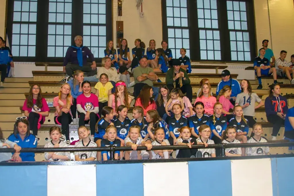 Youth sports team posing in a gymnasium. Many children wearing uniforms, sitting on bleachers