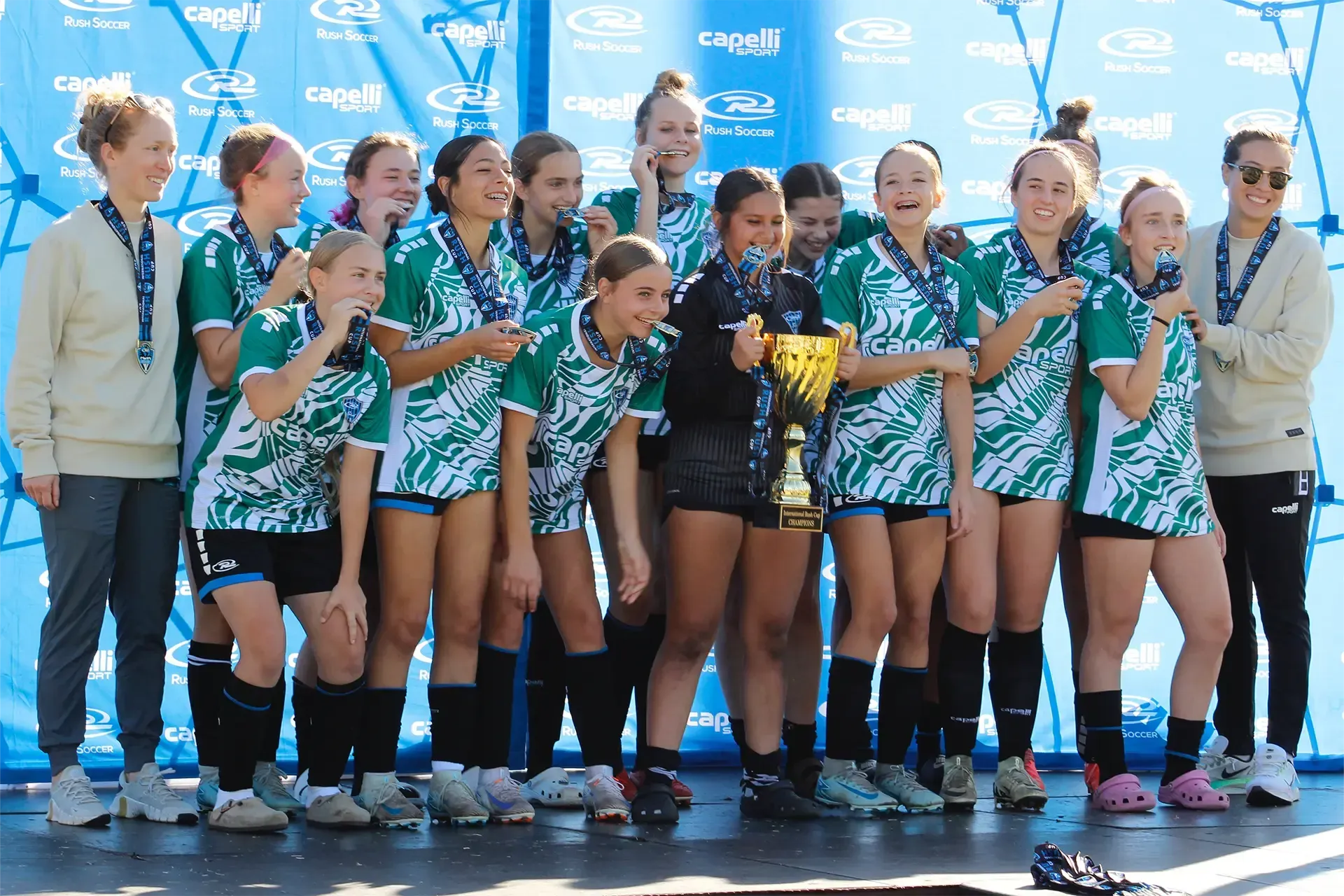 Winning team in green and white jerseys holds a trophy on stage.