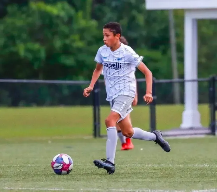Soccer player in a white and gray jersey dribbling a ball on a green field.