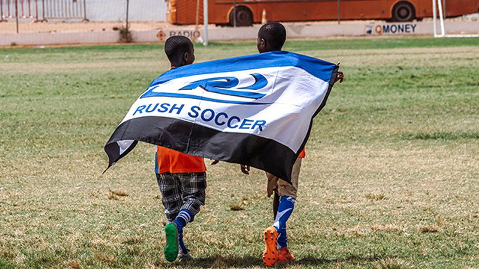 Two children holding a Rush Soccer flag on a grassy field.