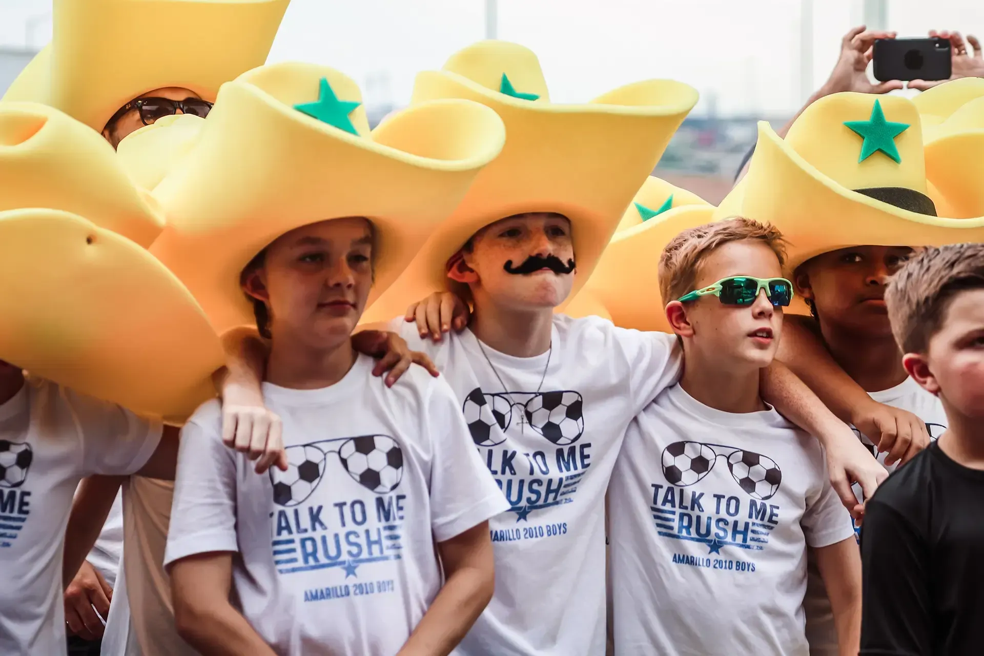 Group of people in large yellow cowboy hats, white shirts, arms around each other.