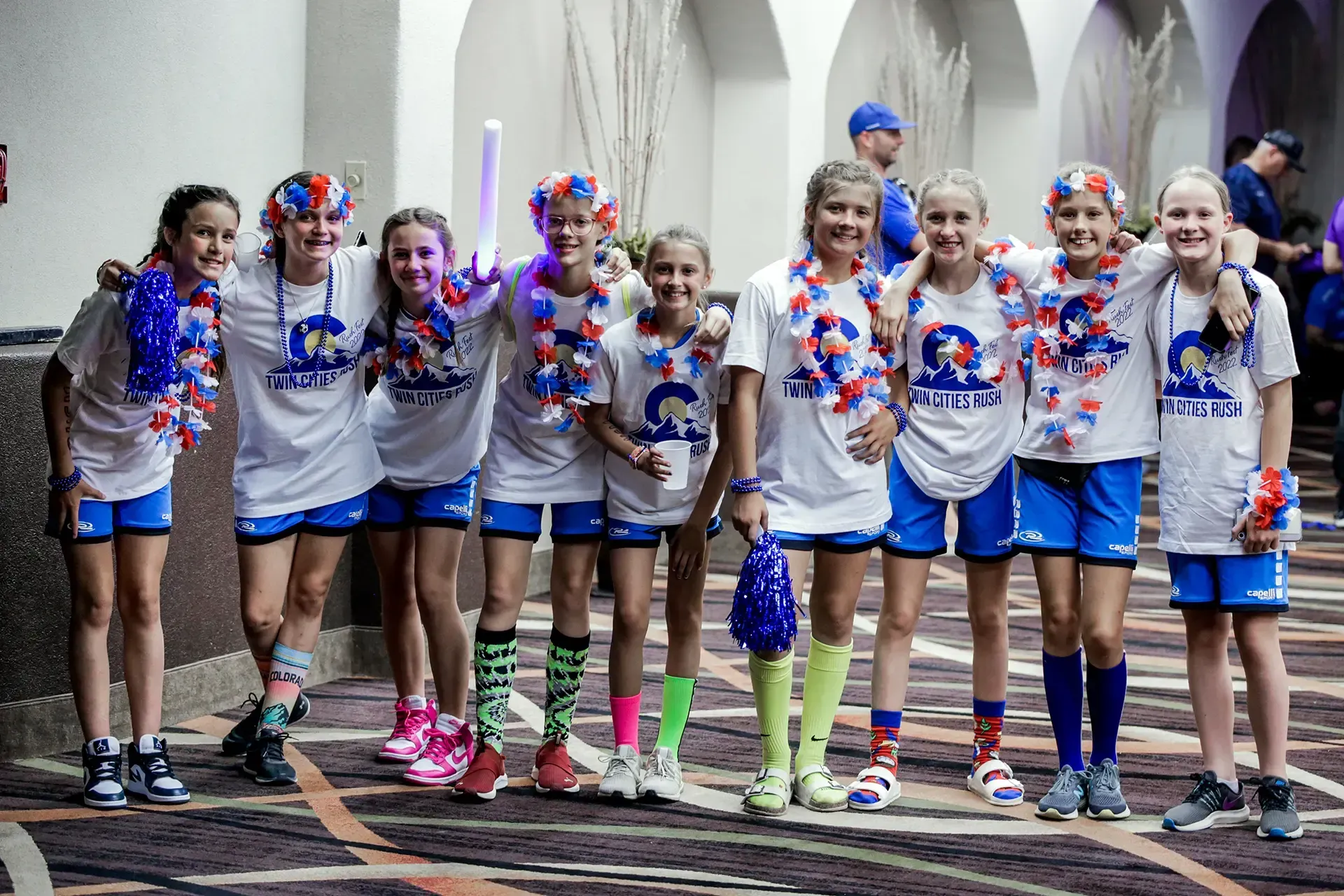 Girls in matching white shirts and blue shorts, posing and smiling, some with decorations.